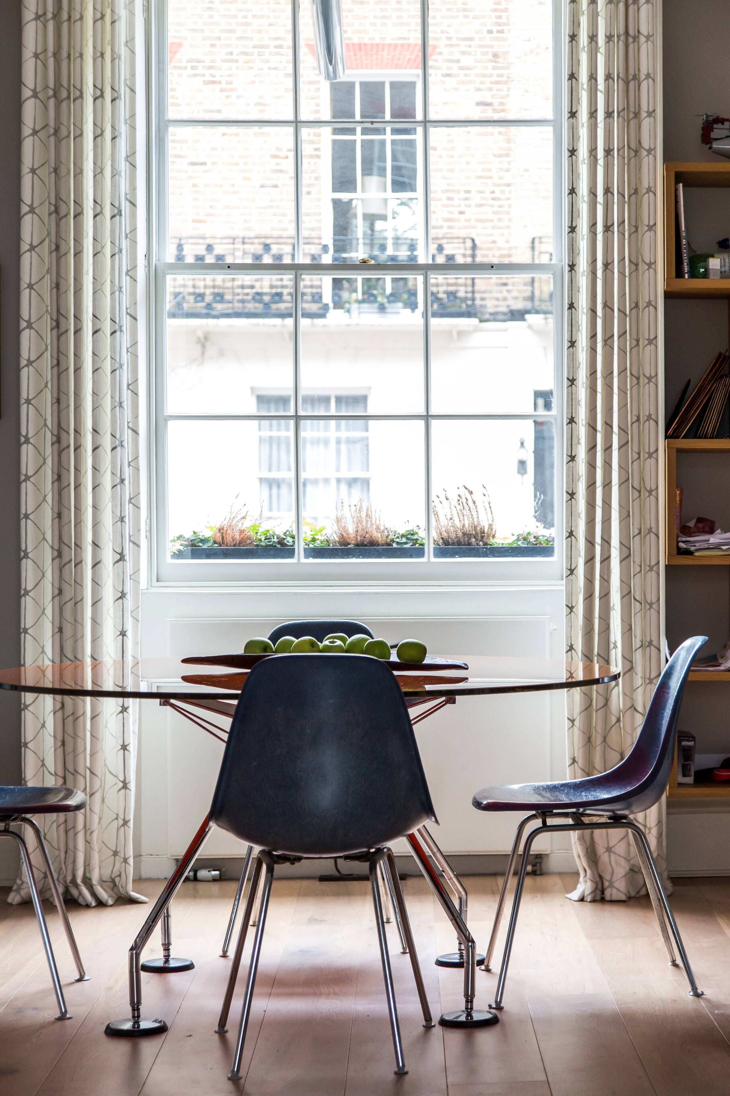 Une pièce comprenant une table à manger, des chaises, une fenêtre avec des rideaux et une bibliothèque.
