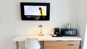 Eine moderne Küche mit Flachbildfernseher über einer weißen Arbeitsplatte, einer Kaffeemaschine, einer Mikrowelle und einem weißen Stuhl.