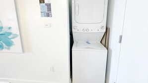 Ein kleiner Hauswirtschaftsraum mit Waschmaschine und Trockner, einer Steckdose und einem Willkommen-Schild an der Wand.