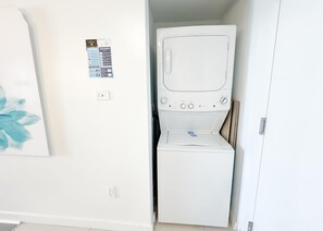A compact laundry room with a washing machine and dryer, a power outlet, and a welcome sign on the wall. - Gorgeous 2BR - Beachwalk Intracoastal View (Hallandale Beach)