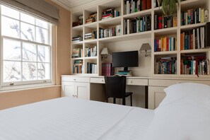 Ein Schlafzimmer mit großem Fenster, Schreibtisch mit Computer, Bücherregal und Bett.
