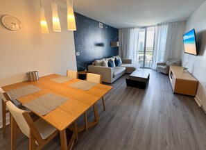 Ein modernes Wohnzimmer mit Essbereich, einer Sofagarnitur, einem Flachbildfernseher und einem großen Fenster mit Blick auf die Stadt.