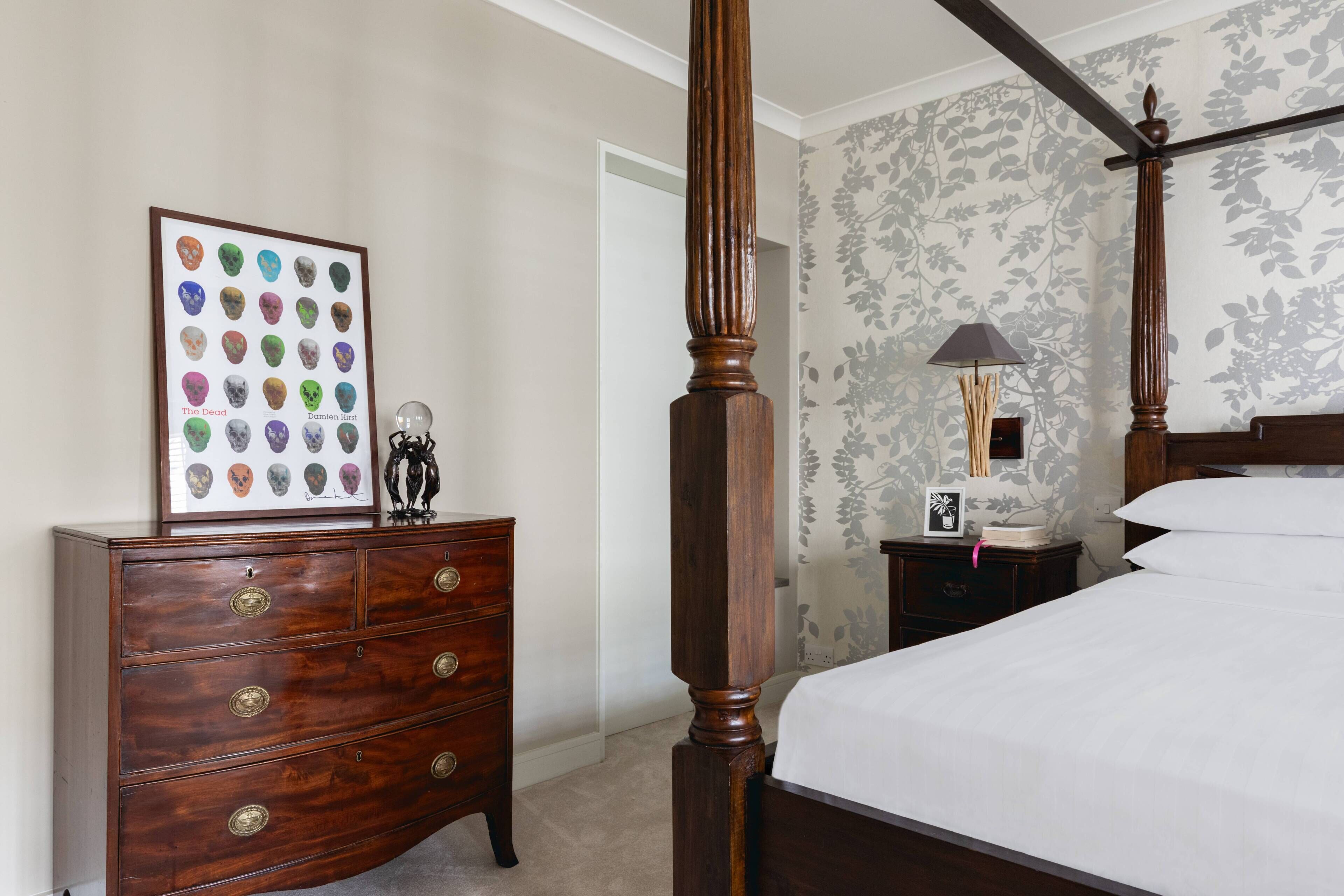 A bedroom with a four-poster bed, a dresser, a framed skull collection, and a nightstand with a lamp.