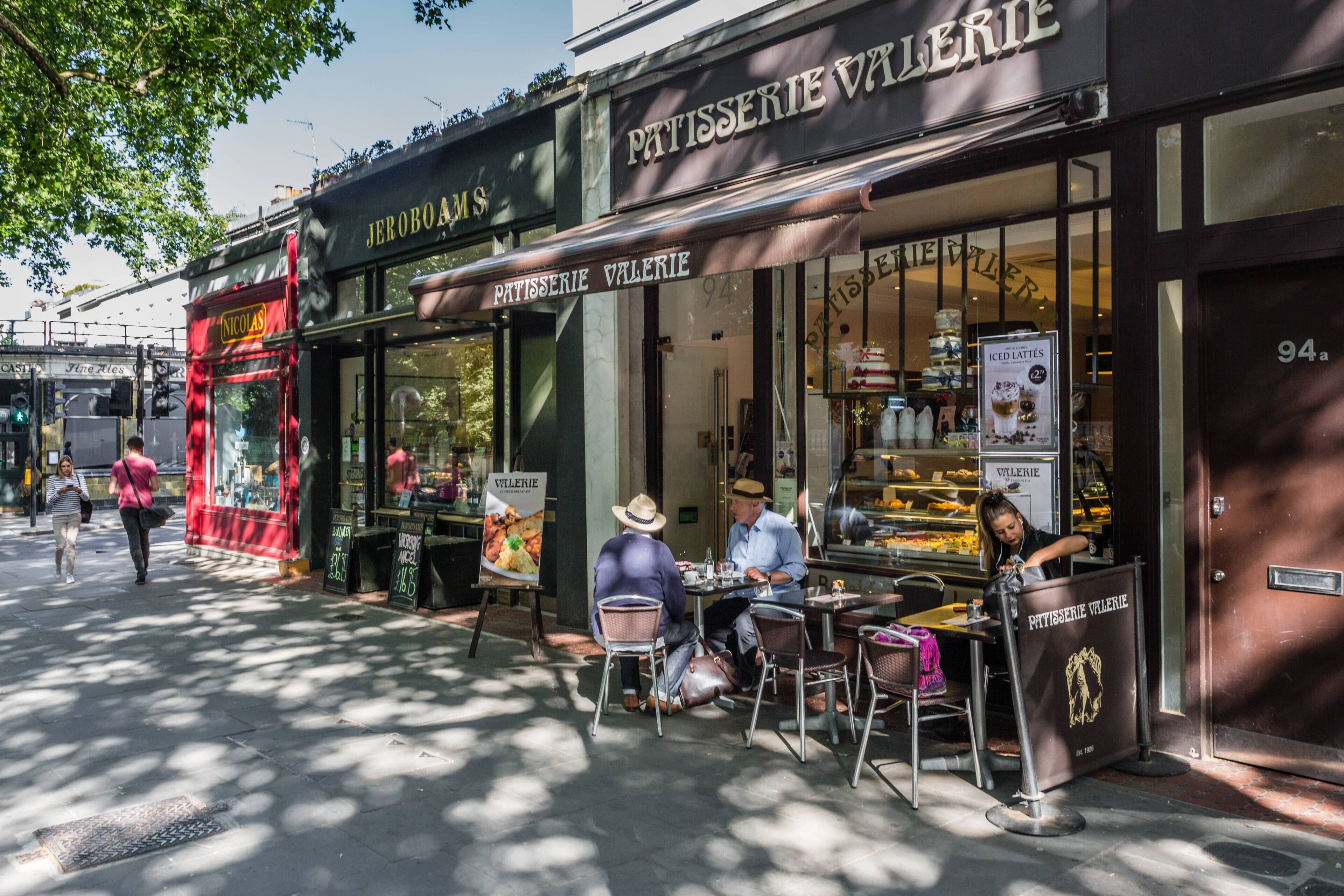 Ein Café mit Außenbereich, ein Geschäft mit der Aufschrift 'Patisserie Valerie' und die Hausnummer 94a ist sichtbar.