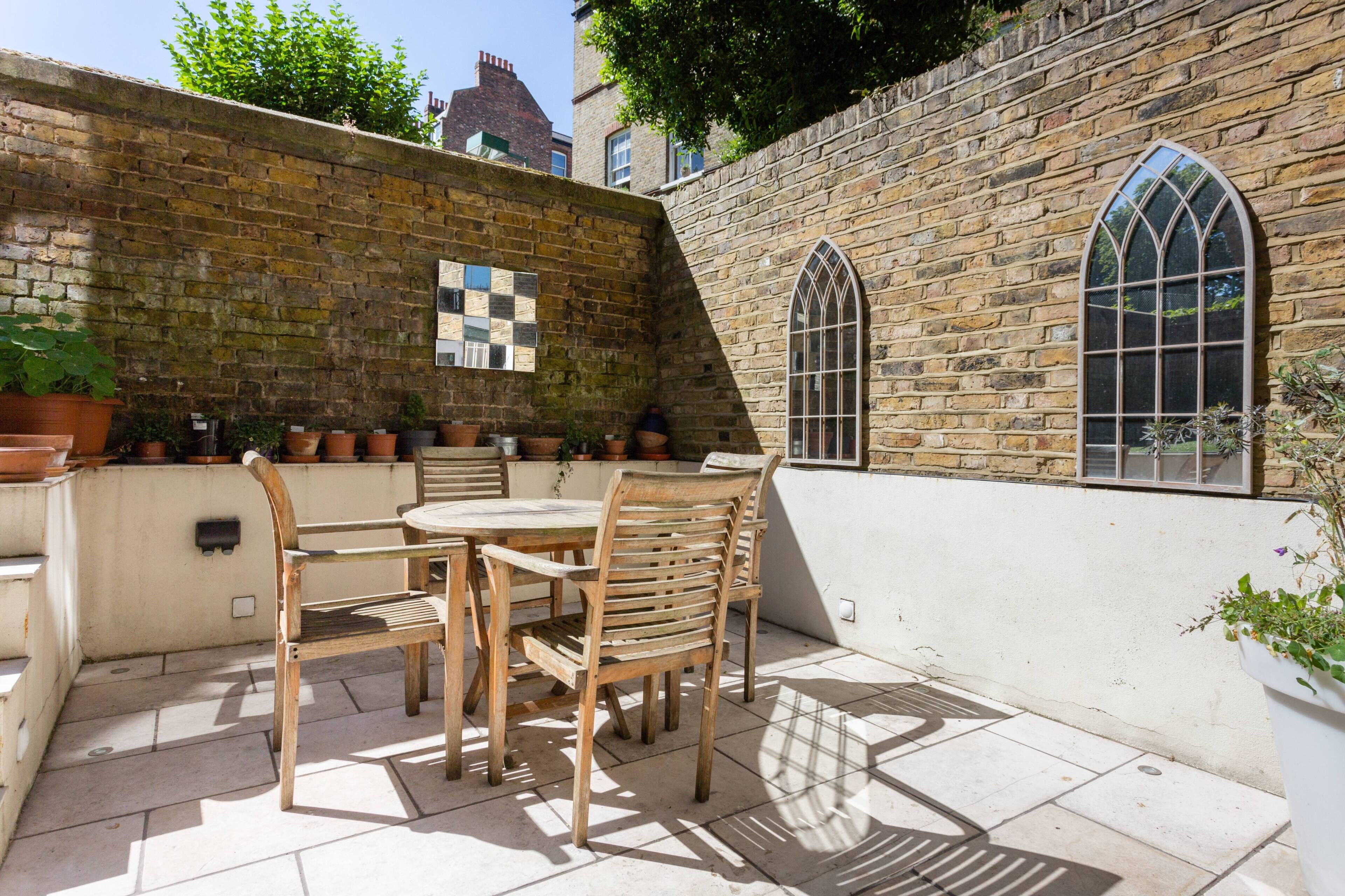 Een terras met een tafel en stoelen, een bakstenen muur en een raam met een geruit patroon.