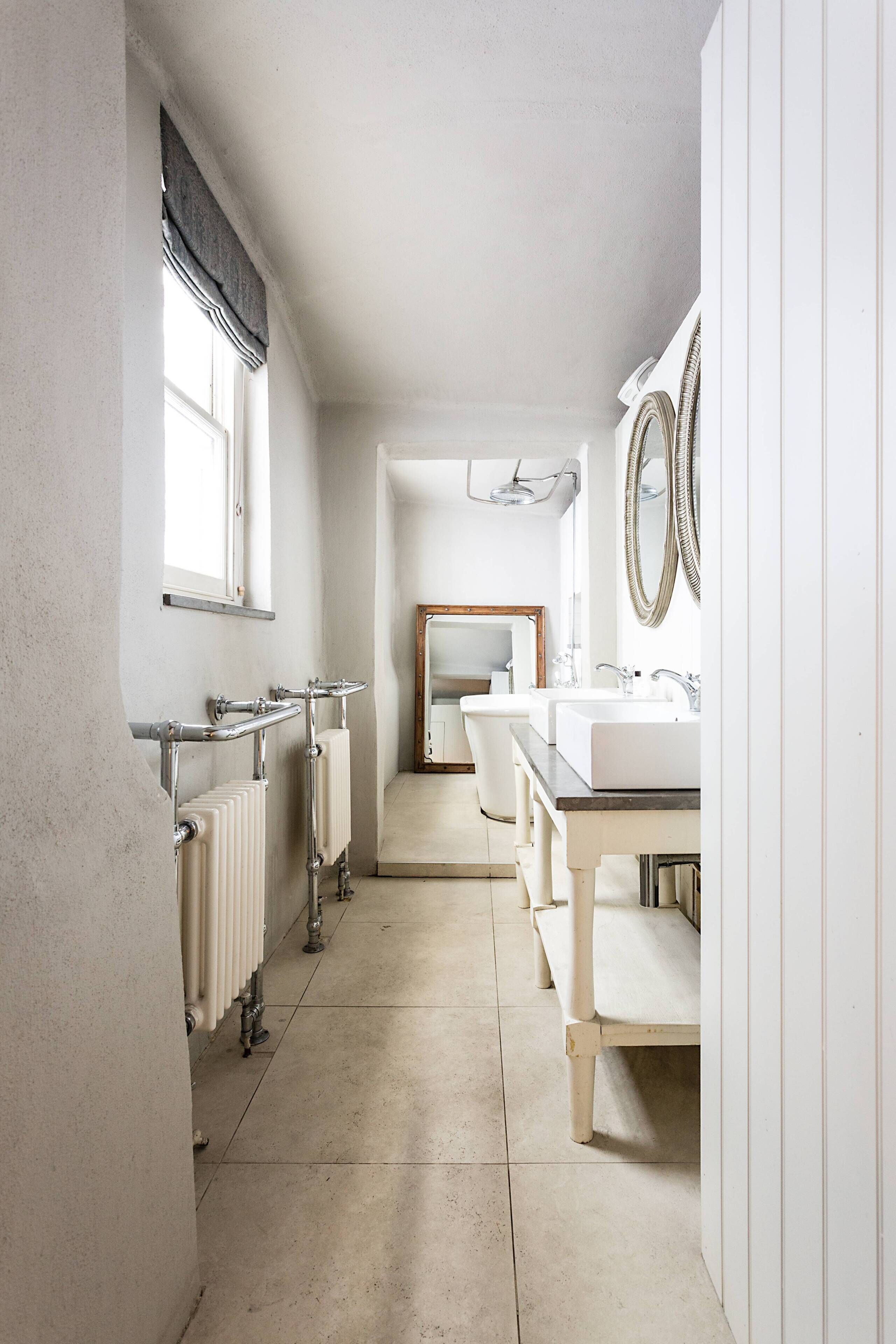 A narrow bathroom with a radiator, a window, a mirror, and a sink.