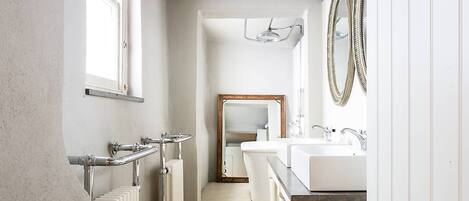A narrow bathroom with a radiator, a window, a mirror, and a sink.