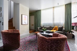Ein Wohnzimmer mit einer Couch, zwei Sesseln, einem Couchtisch, einem gemusterten Teppich und einer Treppe, die in einen anderen Raum führt.