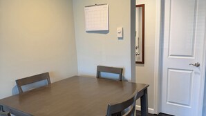 A dining area with a wooden table and four chairs, a wall calendar, a light switch, and a door. - Brilliant, plush studio apartment in Brightwaters,NY .Bars and restaurants 3mins (Brightwaters)