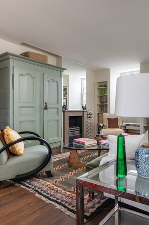 Ein Wohnzimmer mit einer Couch, einem Glastisch, einer Lampe, einem Kamin und einem Bücherregal.