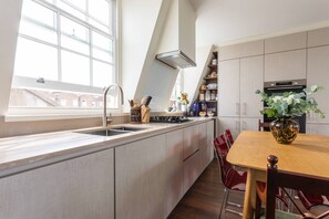 Eine moderne Küche mit einem großen Fenster, einem eingebauten Herd und einem Essbereich mit einem Holztisch und Stühlen.