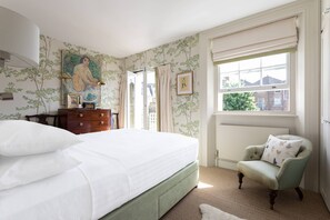 Ein Schlafzimmer mit Bett, Kommode, Stuhl, Fenster und einem Bild an der Wand.