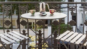 Ein runder Tisch mit zwei Stühlen auf einem Balkon, umgeben von einem schmiedeeisernen Geländer.