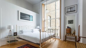 Ein Schlafzimmer mit Bett, Nachttischlampen, einem gemusterten Teppich, einem Fenster mit Aussicht und einer Kommode.