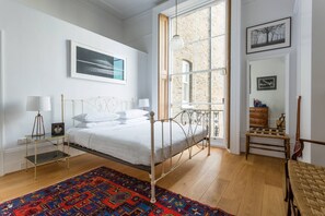 Ein Schlafzimmer mit Bett, Nachttischlampen, einem gemusterten Teppich, einem Fenster mit Aussicht und einer Kommode.