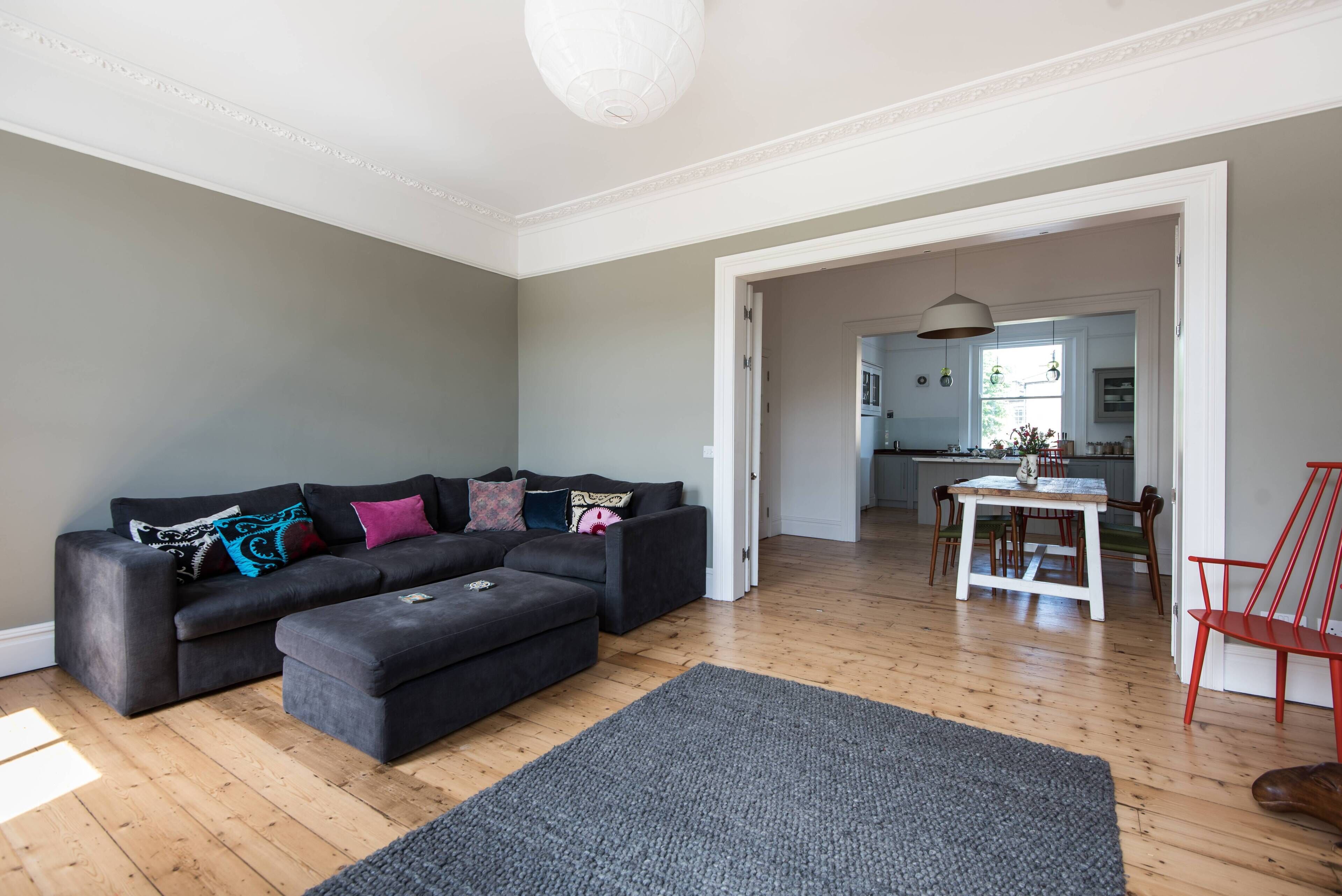 A living room with a grey sofa, ottoman, and a dining area with a table and chairs.
