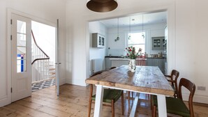 A dining area with a wooden table and chairs, a staircase, and a kitchen in the background. - Westbourne Grove VIII (London)