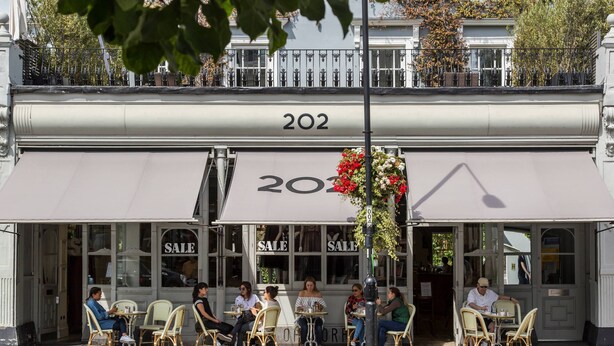 A cafe with outdoor seating, a sale sign, and a number '202' on the awning. - Westbourne Grove VIII (London)