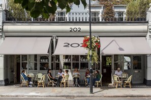 Café com mesas ao ar livre, um aviso de promoção e o número '202' na marquise.