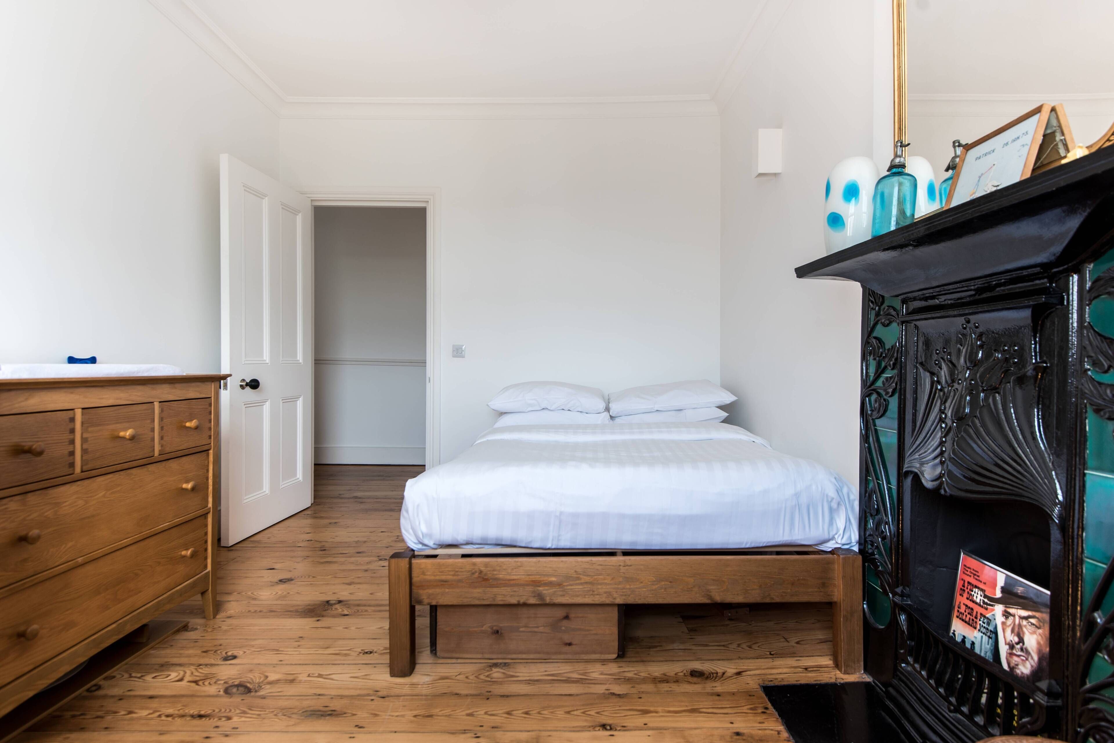 Ein Schlafzimmer mit einem hölzernen Bett, einem Schminktisch, einem Kamin und einer Tür zu einem weiteren Raum.