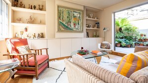 Ein Wohnzimmer mit einem roten Sessel, einem beigen Sofa, einem Glastisch und Regalen mit Dekoration.