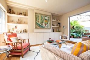 A living room with a red chair, a beige sofa, a glass coffee table, and shelves with decorative items. - Wyndham Mews III - Three Bedroom House, Sleeps 6 (London)