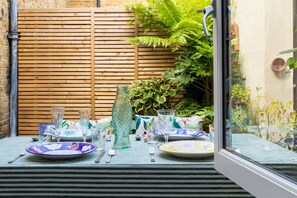A dining table set with plates, glasses, and cutlery, a fish-shaped vase, and a wooden fence in the background. - Wyndham Mews III - Three Bedroom House, Sleeps 6 (London)