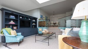 A living room with a sofa, armchair, coffee table, and a bookshelf. - Granard Road - Four Bedroom House, Sleeps 8 (London)