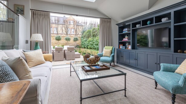 A modern living room with a glass coffee table, a sofa, a teal armchair, and a grey cabinet with shelves. - Granard Road - Four Bedroom House, Sleeps 8 (London)