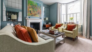 A living room with a fireplace, two armchairs, a sofa, and a large painting on the wall. - Granard Road - Four Bedroom House, Sleeps 8 (London)