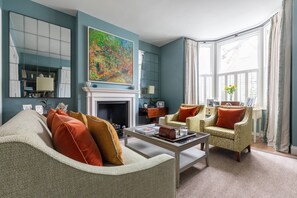 Ein Wohnzimmer mit Kamin, zwei Sesseln, einem Sofa und einem großen Gemälde an der Wand.