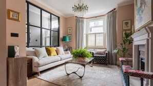 Ein Wohnzimmer mit einer Couch, einem Couchtisch mit einer Pflanze, einem Kamin und einem großen Fenster mit Vorhängen.