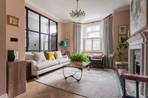 Ein Wohnzimmer mit einer Couch, einem Couchtisch mit einer Pflanze, einem Kamin und einem großen Fenster mit Vorhängen.
