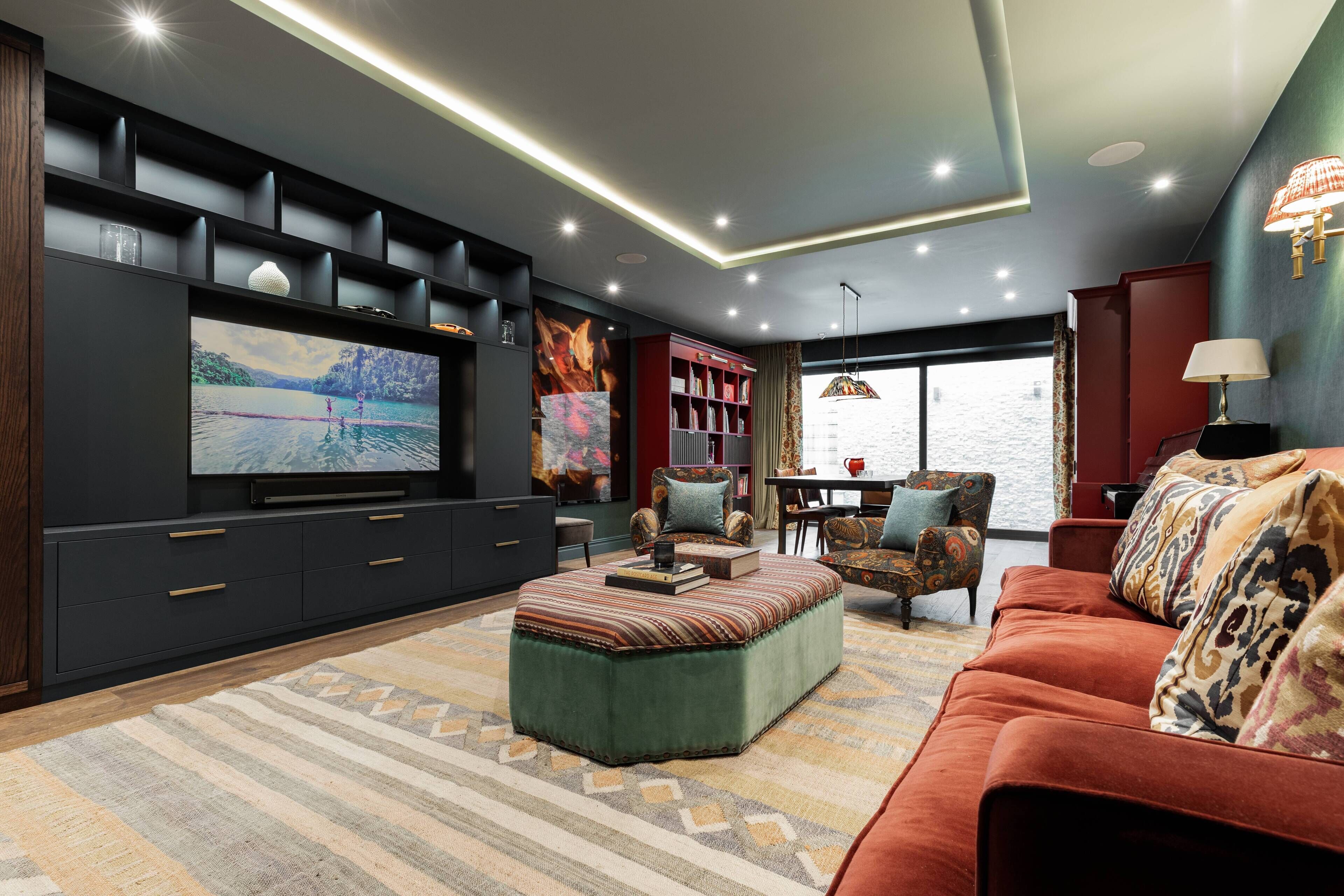 A modern living room with a flat-screen TV, a sofa, ottoman, and a dining area with chairs and a table.