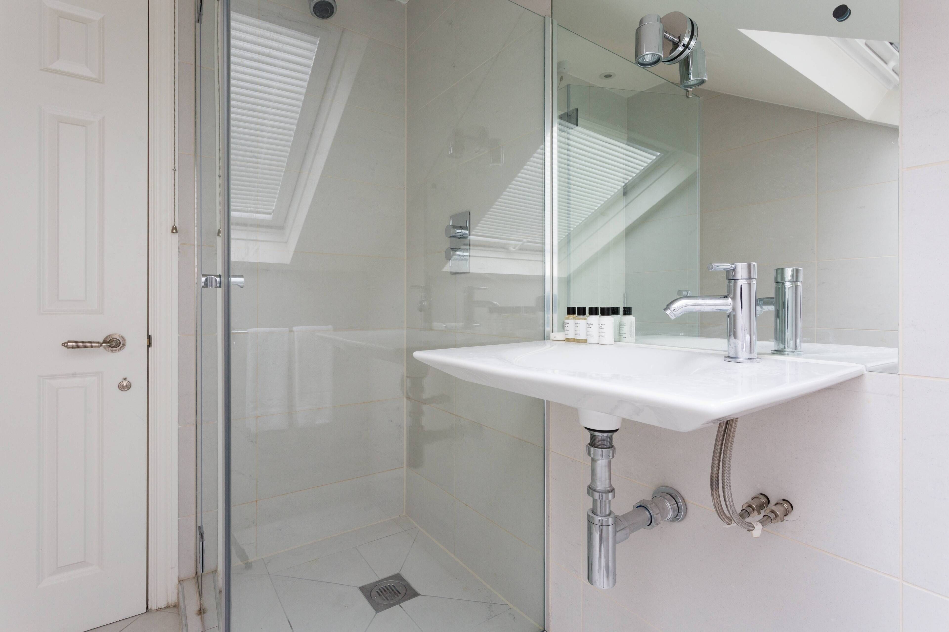 A modern bathroom with a glass shower enclosure, a white sink, and a mirror.