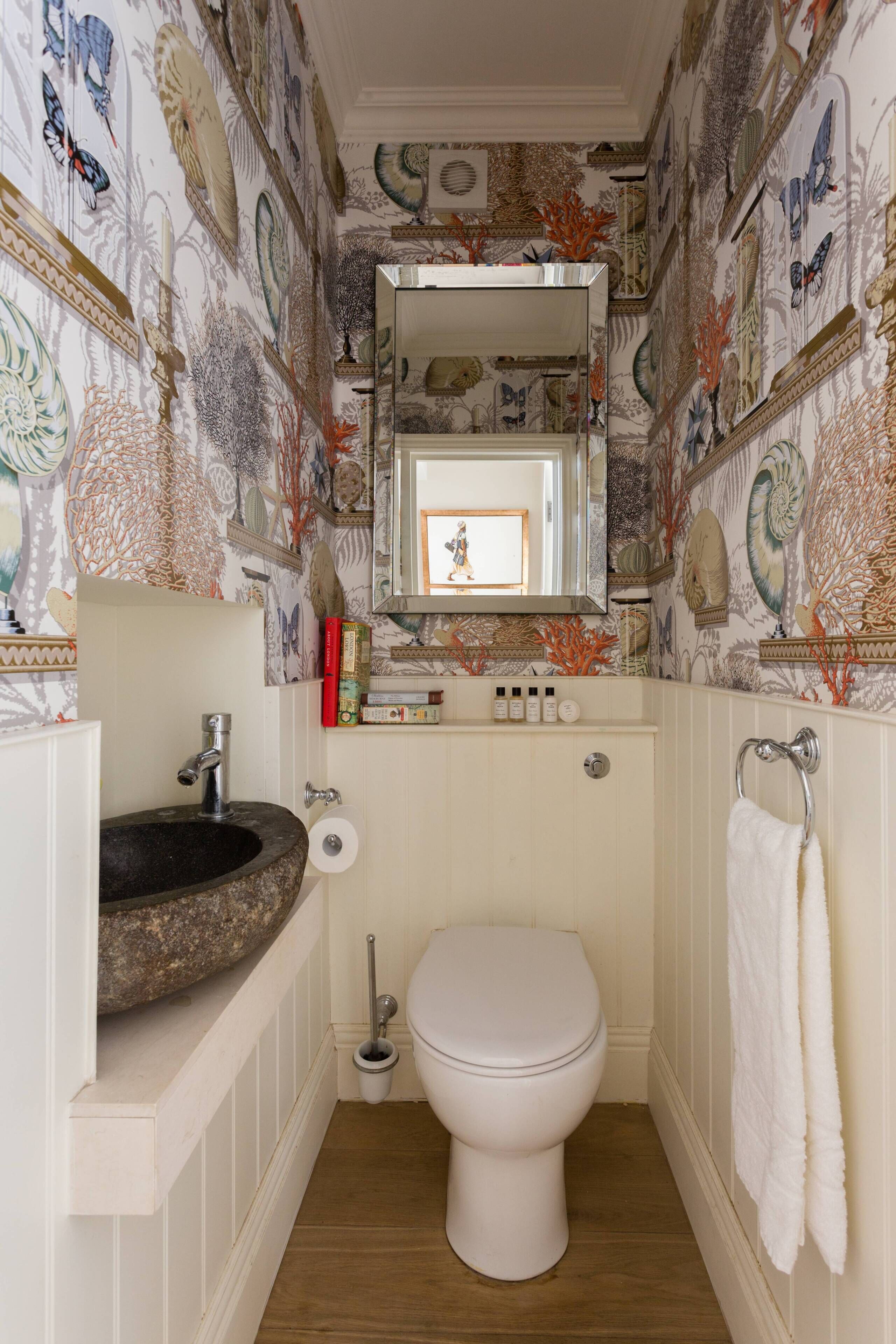 Un bagno con lavandino in pietra, water bianco e carta da parati decorata.