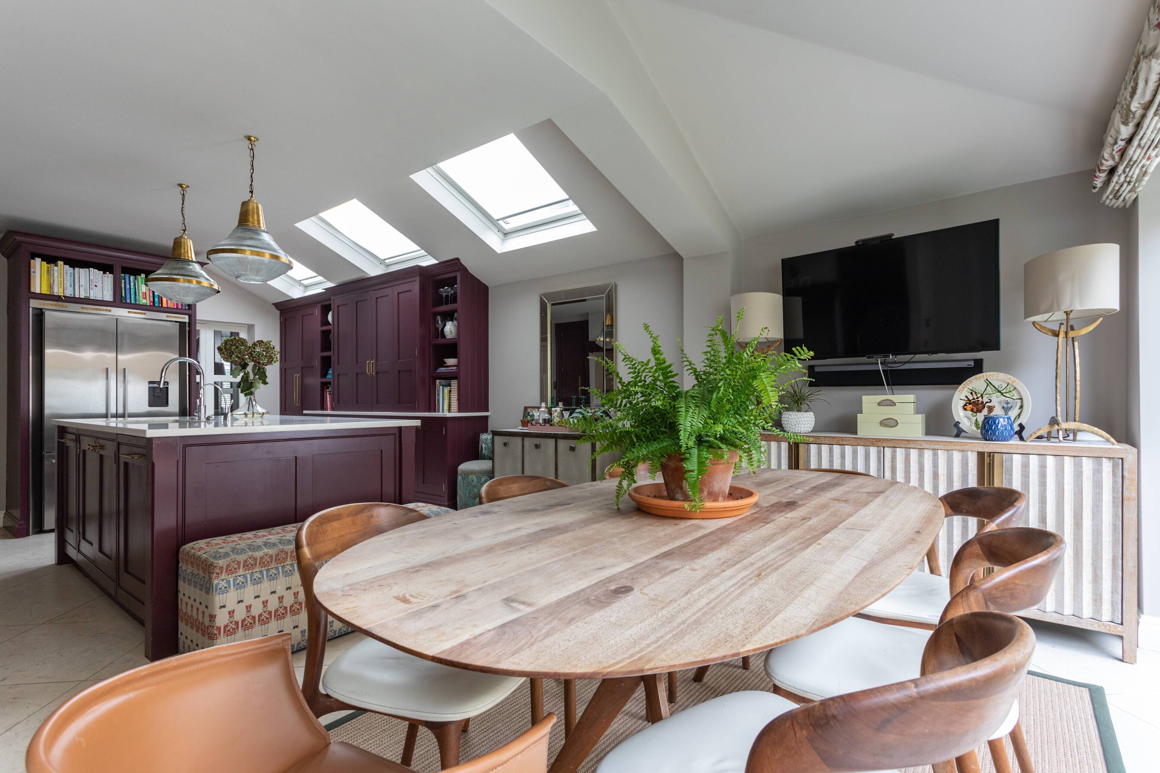 Une cuisine moderne avec des fenêtres de toit, un coin repas doté d’une table en bois et un téléviseur fixé au mur.