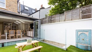 Eine moderne Terrasse mit Pool, Holzmöbeln und einer Glastür zu einem überdachten Bereich.