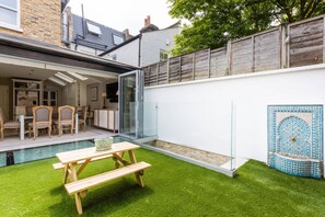 Eine moderne Terrasse mit Pool, Holzmöbeln und einer Glastür zu einem überdachten Bereich.