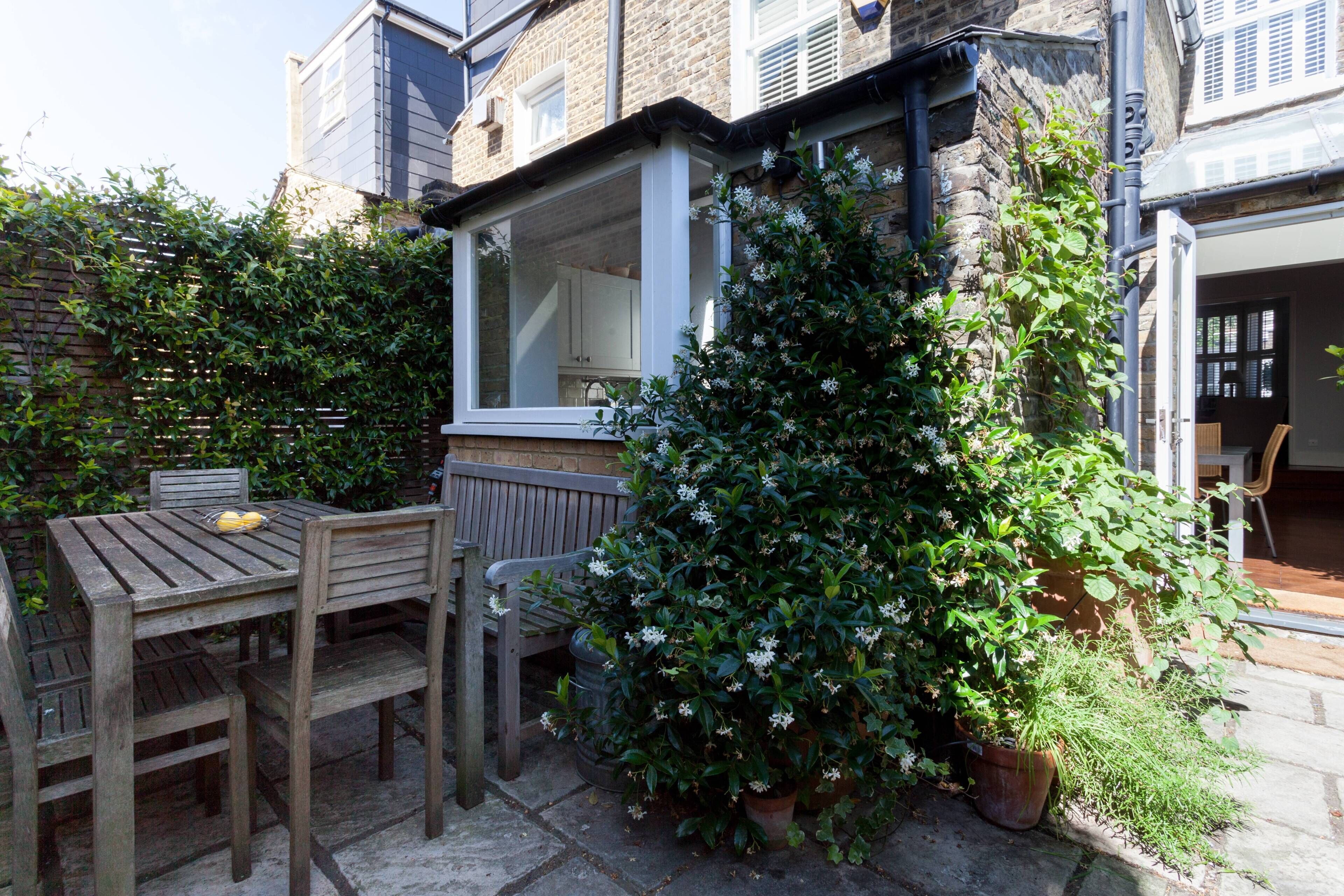 A wooden table and chairs outside a house with a window and a potted plant.