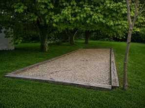 Ein rechteckiger Außenbereich mit Holzumrandung, umgeben von Gras und Bäumen.
