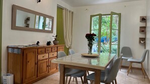 Un coin repas comprenant un buffet en bois, une table avec des chaises, un vase avec des fleurs et une fenêtre donnant sur un paysage verdoyant.