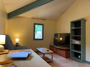 Ein Zimmer mit einem Bett, einem Schreibtisch mit Lampe, einem Fernseher, einem Fenster und einem Bücherregal.
