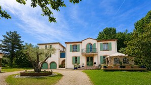 Un bâtiment à deux étages avec une allée en gravier, des volets verts et un jardin avec un arbre.