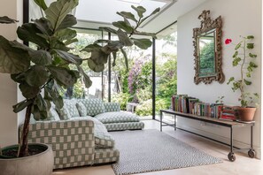 Ein modernes Wohnzimmer mit einer Couch, einer großen Topfpflanze, einem Bücherregal und einem Spiegel.