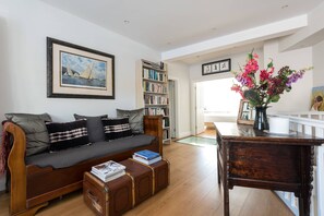 Ein Wohnzimmer mit einer Couch, einem Bücherregal, einem Holztisch und einer Blumenvase.