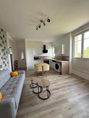 Eine moderne Küche mit einer zentralen Kochinsel, einem Essbereich mit rundem Tisch und einem grauen Sofa mit Kürbisdeko.