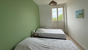 Et soveværelse med to senge, et vindue med udsigt, en hængende lampe og et billede på væggen.