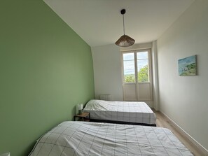 Ein Schlafzimmer mit zwei Betten, einem Fenster mit Aussicht, einer hängenden Leuchte und einem Bild an der Wand.