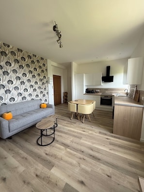 Un salon moderne avec un canapé gris, une petite table ronde et un mur orné d’un motif.